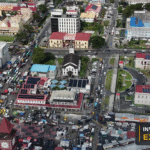 Drone view of Stabroek Market and central Georgetown, with the Invest Guyana Explains masthead.