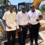 Three BIT graduates holding certificates beside heavy-duty equipment in Region Three