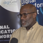 A speaker being interviewed in front of Saint Lucia DigiGov and national authentication displays.