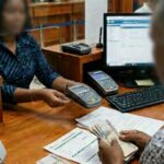 A Guyana Development Bank teller assists a customer handling Guyanese currency and banking documents.