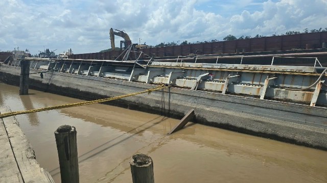 A waste-oil barge lists at an East Bank of Demerara wharf as authorities respond to a potential spill risk.